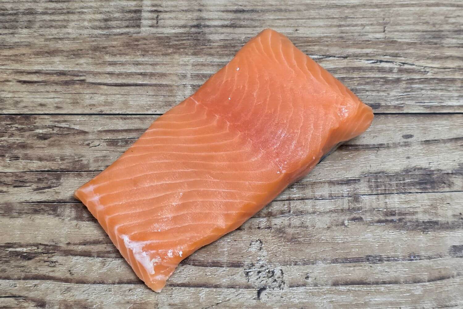 Raw Wild Alaskan king salmon fillet portion on a rustic wood surface.