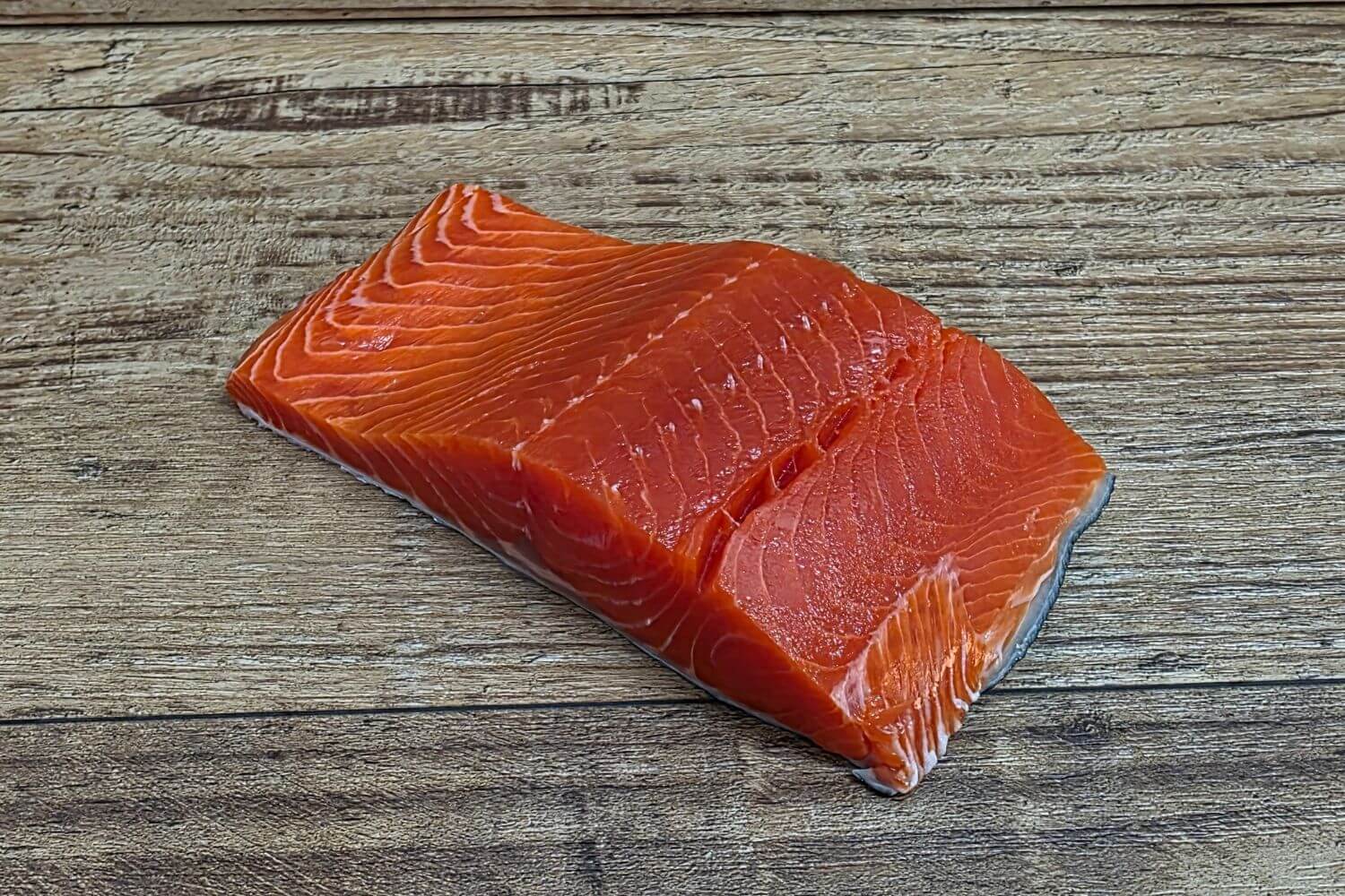 Sushi-grade sockeye salmon portion on rustic wood.
