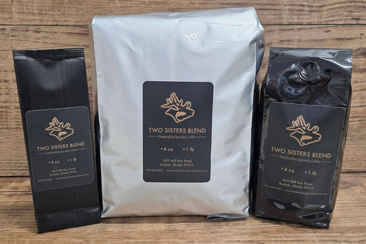 Three packages of Two Sisters Blend coffee from Kodiak Island Smokehouse on a wooden surface.