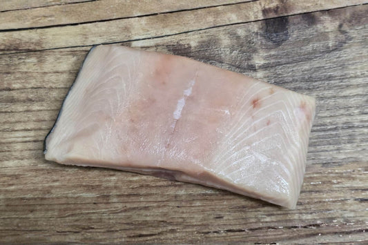 Single raw Wild Alaskan white king salmon fillet portion displayed on a rustic wooden background, showing its pale ivory flesh, subtle marbling, and natural sheen.