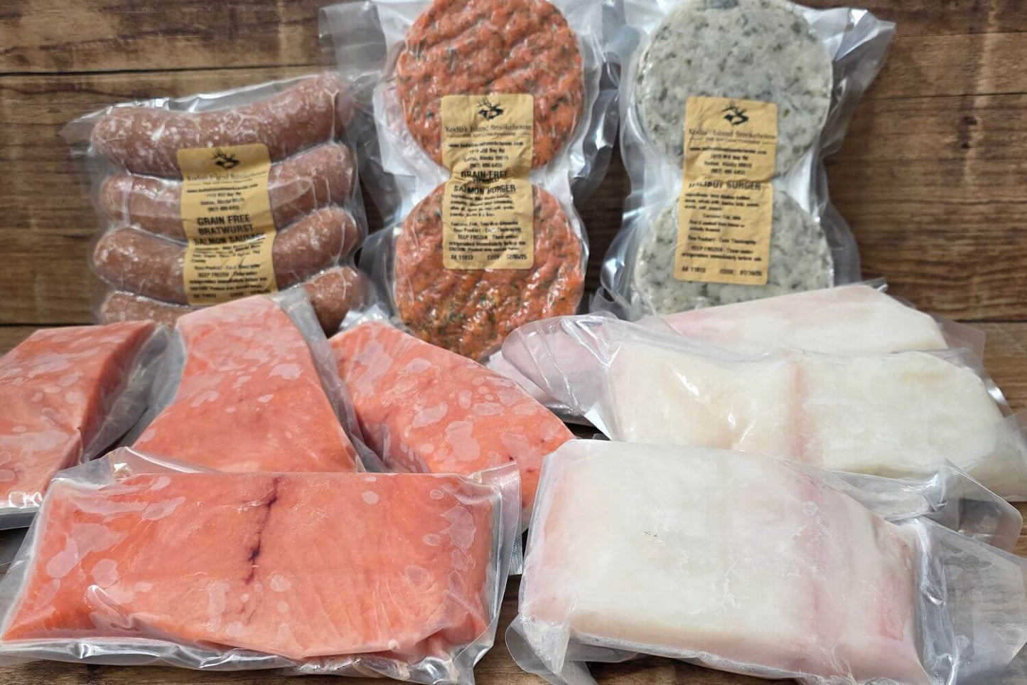 Assorted packaged seafood including salmon sausages, king salmon, & halibut on a wooden surface.