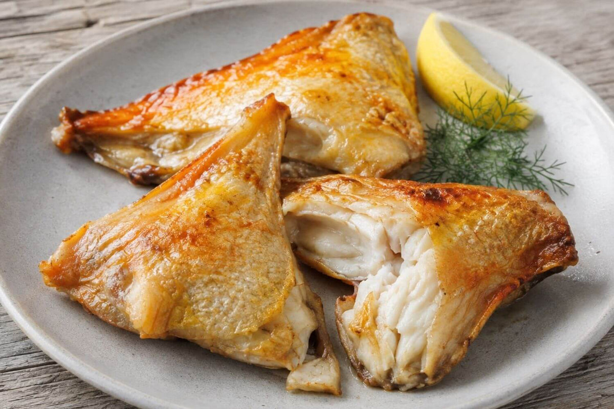 Cooked wild Alaska yelloweye collars with golden crisped skin and moist white flakes, served with lemon and dill on a rustic wooden table.