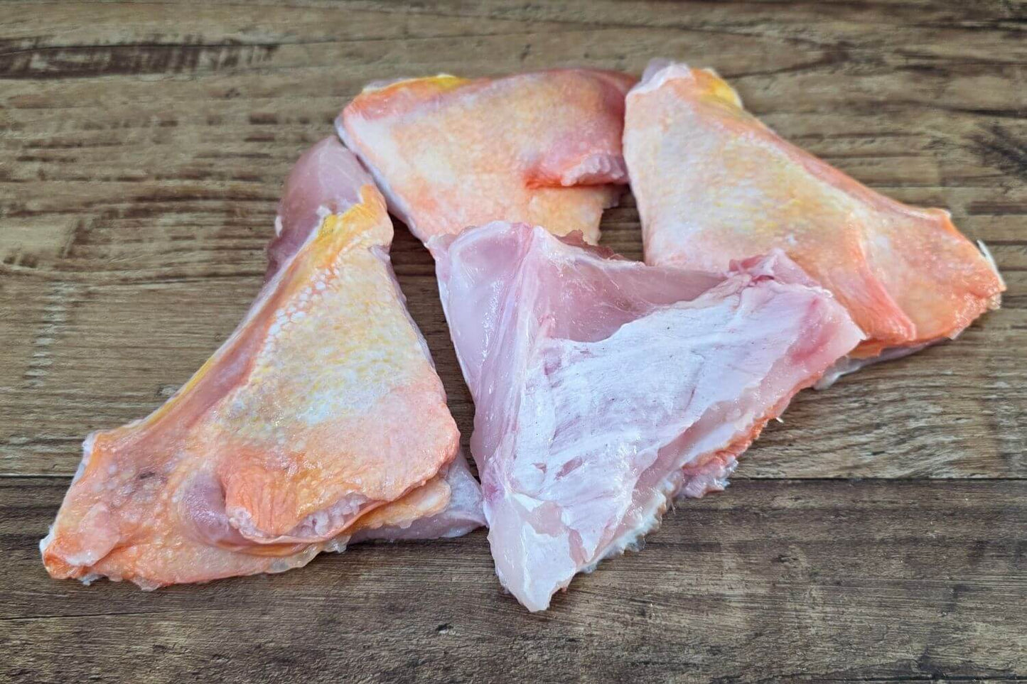 Raw wild Alaska yelloweye collars showing their naturally pink-white flesh and distinctive golden-orange skin on a rustic wooden surface.