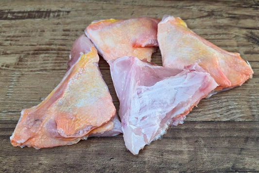 Raw wild Alaska yelloweye collars showing their naturally pink-white flesh and distinctive golden-orange skin on a rustic wooden surface.