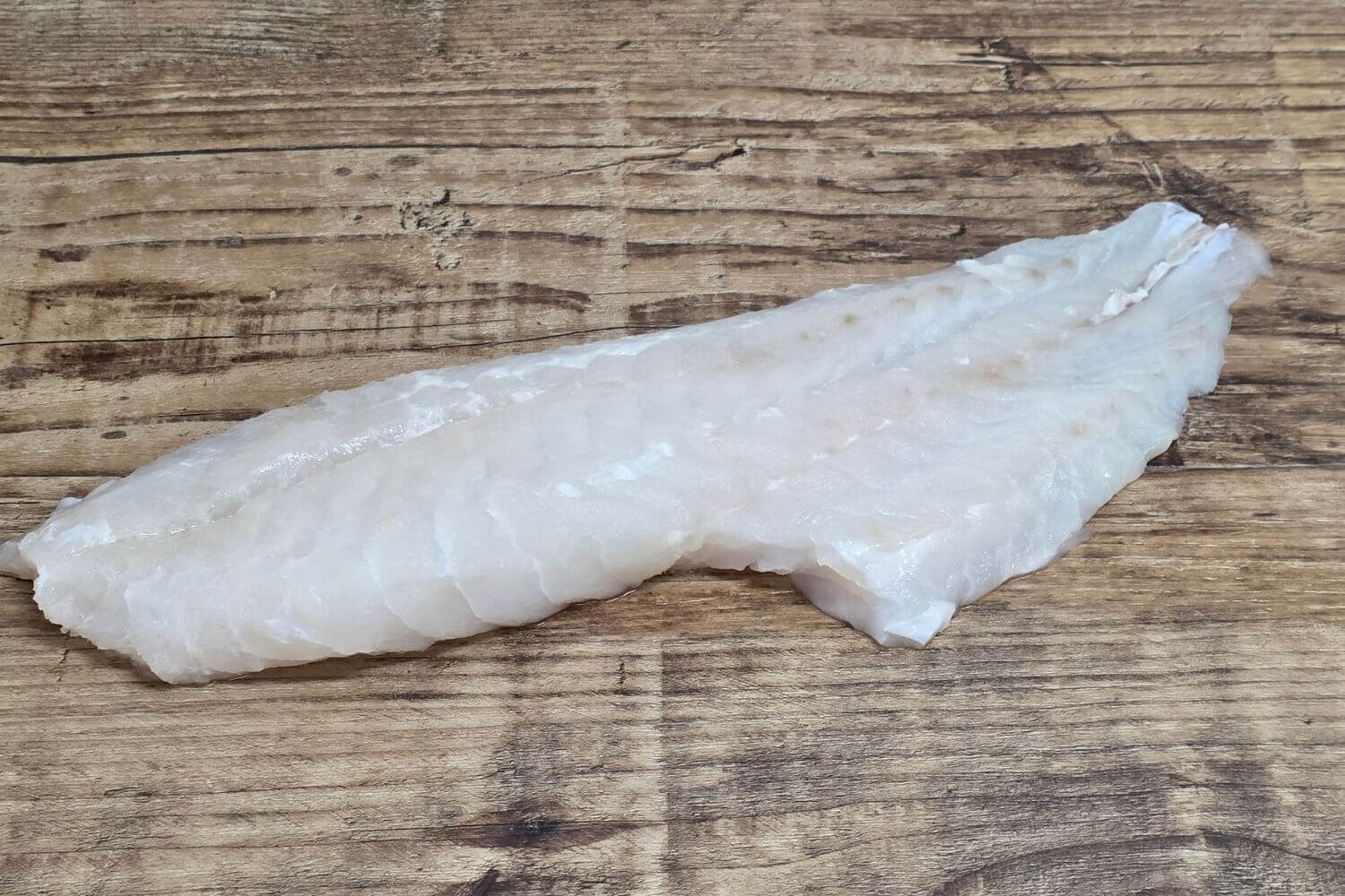 Skinless yelloweye rockfish fillet on rustic wood surface.